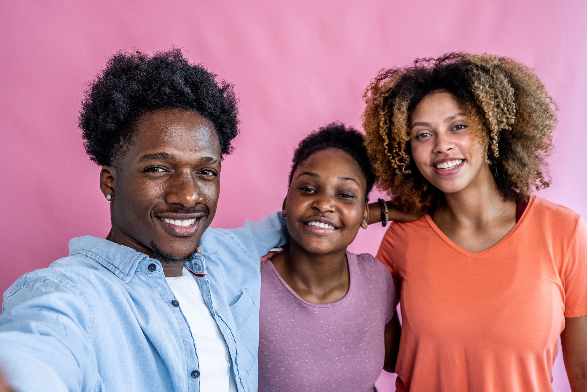 Young man taking a selfie of his friends on a pink background